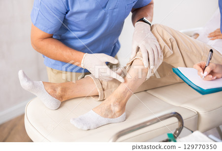 Cropped male doctor shows problem areas of varicose veins on mature woman patients leg. Cropped male doctor shows problem areas of varicose veins on mature woman patients leg. 129770350