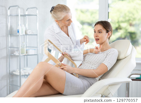 Young woman having consultation about face aesthetic while looking in the mirror 129770357