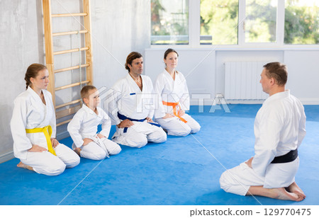 Family in gym at group karate training with trainer are in sitting position Family in gym at group karate training with trainer are in sitting position 129770475