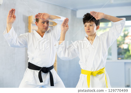 Teen boy and middle-aged man wearing kimono training karate techniques 129770499