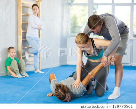 At self-defense training, trainer teaches teenage girl technique of grabbing arm and lowering opponent to floor At self-defense training, trainer teaches teenage girl technique of grabbing arm and lowering opponent to floor 129770501