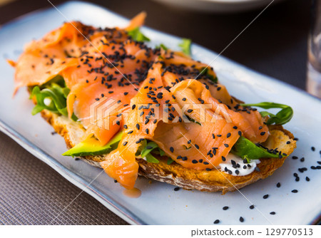 Delicious smoked salmon with arugula avocado and seeds on fried bread Delicious smoked salmon with arugula avocado and seeds on fried bread 129770513