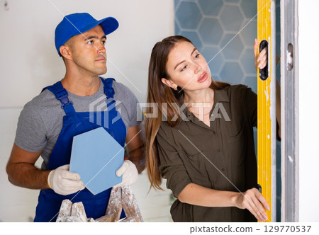 Owner of apartment checks verticality of wall, made by professional builder, using building level 129770537