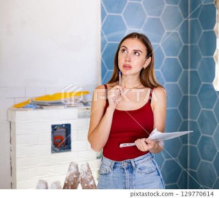Portrait of young client woman with documents in hands checks quality of completed repairs Portrait of young client woman with documents in hands checks quality of completed repairs 129770614