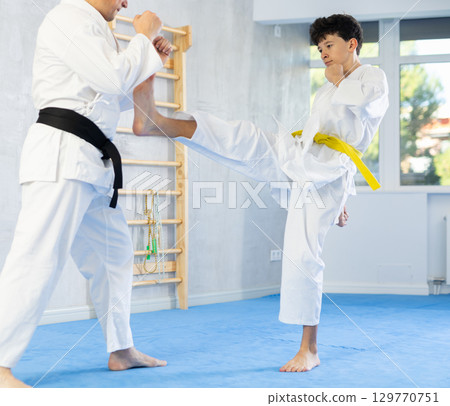 Karate lesson for teenager - guy and trainer are sparring in gym Karate lesson for teenager - guy and trainer are sparring in gym 129770751