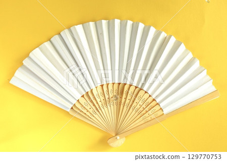 White folding fan on yellow background White folding fan on yellow background 129770753