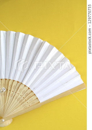 White folding fan on yellow background White folding fan on yellow background 129770755