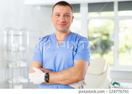 Middle-aged man doctor stands with arms crossed on chest in hospital office Middle-aged man doctor stands with arms crossed on chest in hospital office 129770791