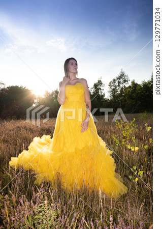 A Stunning Woman Wearing a Beautiful Yellow Dress Posed Gracefully Against a Vibrant Sunset 129771034