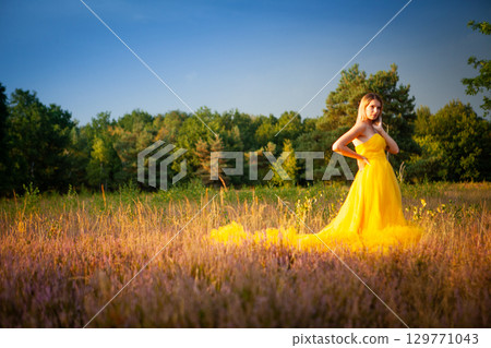 An Elegant Woman in a Beautiful Yellow Dress Strolling Through a Serene Meadow During Summer 129771043