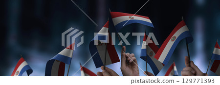 Paraguay flags in their hands on a blurred urban background 129771393