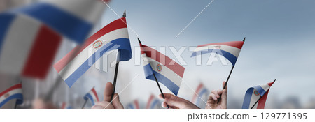 Paraguay flags in their hands on a blurred urban background 129771395