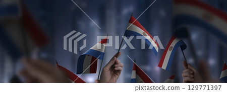 Paraguay flags in their hands on a blurred urban background 129771397