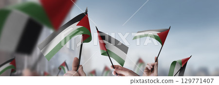 Palestine flags in their hands on a blurred urban background 129771407