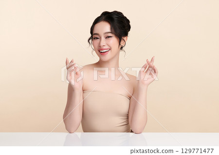 A beautiful young Asian woman with clean, fresh skin against a beige background. Skincare, facial treatment, cosmetology, beauty, and spa. An elegant portrait of an Asian woman. 129771477