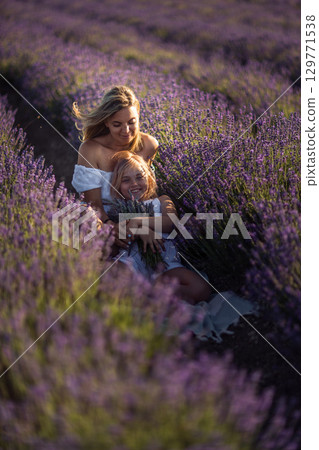 Lavender Mother Daughter: Sitting, embracing in a vast lavender field at sunset for cherished family memories. Lavender Mother Daughter: Sitting, embracing in a vast lavender field at sunset for cherished family memories. 129771538