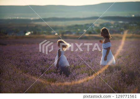 Lavender field Mother daughter Sunset: Two women in white dresses enjoying golden hour in vast lavender field with distant hills. Lavender field Mother daughter Sunset: Two women in white dresses enjoying golden hour in vast lavender field with distant hills. 129771561