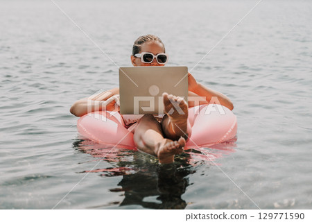 A woman is floating in a pink inflatable raft with a laptop in her hand. She is smiling and she is enjoying her time in the water. A woman is floating in a pink inflatable raft with a laptop in her hand. She is smiling and she is enjoying her time in the water. 129771590