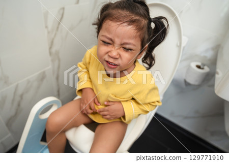 toddler girl sitting on toilet at home and suffering from stomachache and constipation 129771910
