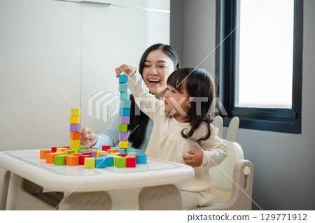 happy toddler girl playing wooden block toy cubes with her mother on table happy toddler girl playing wooden block toy cubes with her mother on table 129771912