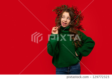 Young girl in green sweater biting a candy cane 129772323