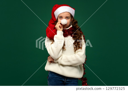 Girl in Santa hat holding pompom to nose Girl in Santa hat holding pompom to nose 129772325