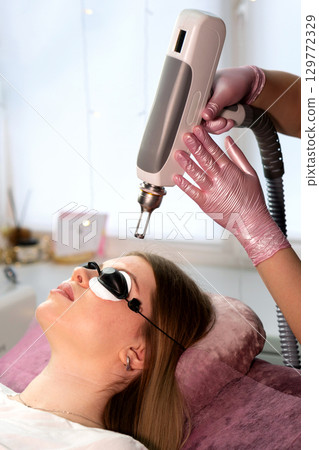 Technician positions laser above closed eyes for eyebrow tattoo removal Technician positions laser above closed eyes for eyebrow tattoo removal 129772329