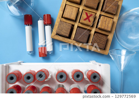 Closeup view of an empty test tube with a wooden tic tac toe game on a blue background. Mockup or Copy space. Concept of healthcare and medicine Closeup view of an empty test tube with a wooden tic tac toe game on a blue background. Mockup or Copy space. Concept of healthcare and medicine 129772569