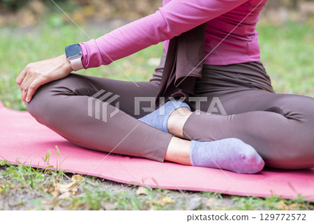 Woman in a sporty outfit practices yoga on a fitness mat in a public park outdoors. Concept of a Healthy active lifestyle Woman in a sporty outfit practices yoga on a fitness mat in a public park outdoors. Concept of a Healthy active lifestyle 129772572