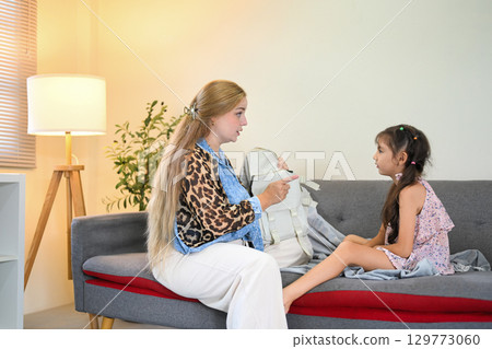 Little girl showing unwillingness to go to school as her mother holds a backpack Little girl showing unwillingness to go to school as her mother holds a backpack 129773060