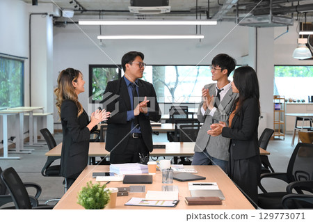 Group of business professionals congratulating a team member in a modern office Group of business professionals congratulating a team member in a modern office 129773071