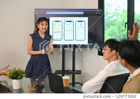 Confident woman giving a presentation on mobile UI UX design to colleagues in a modern office Confident woman giving a presentation on mobile UI UX design to colleagues in a modern office 129773092