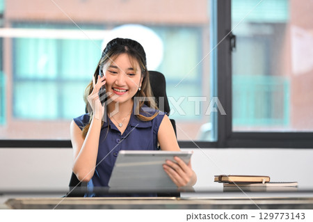 Businesswoman having a conversation on phone and working with digital tablet Businesswoman having a conversation on phone and working with digital tablet 129773143