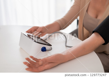 Close up of womans arm in cuff while checking blood pressure with electronic monitor in cozy modern apartment, health monitoring and care Close up of womans arm in cuff while checking blood pressure with electronic monitor in cozy modern apartment, health monitoring and care 129773247