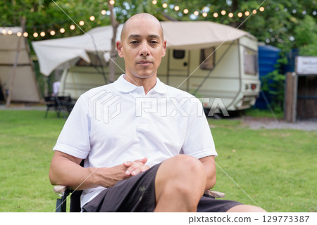 Confident bald man relaxing at campsite with camper van in outdoor travel lifestyle scene 129773387