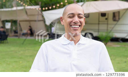 Confident bald man relaxing at campsite with camper van laughing with eyes closed Confident bald man relaxing at campsite with camper van laughing with eyes closed 129773396