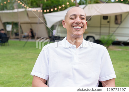 Confident bald man relaxing at campsite with camper van laughing with eyes closed 129773397