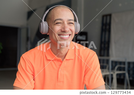 Man listening music with headphones in coffee shop restaurant while smiling 129773434