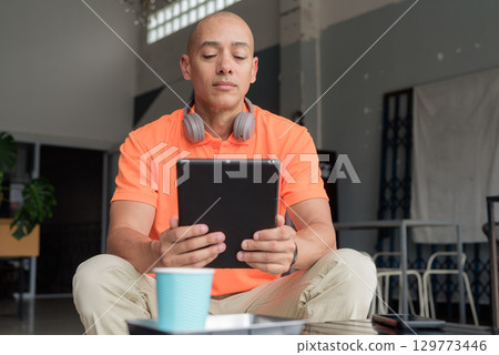 Bald Hispanic man using digital tablet computer in coffee shop Bald Hispanic man using digital tablet computer in coffee shop 129773446