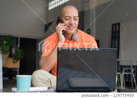 Bald Hispanic man sitting and using laptop computer and phone in coffee shop restaurant Bald Hispanic man sitting and using laptop computer and phone in coffee shop restaurant 129773450