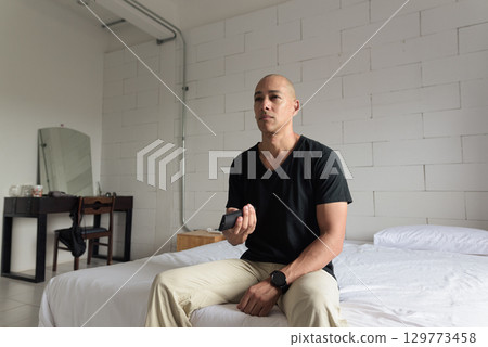 Man sitting and watching television at home while sitting on bed 129773458