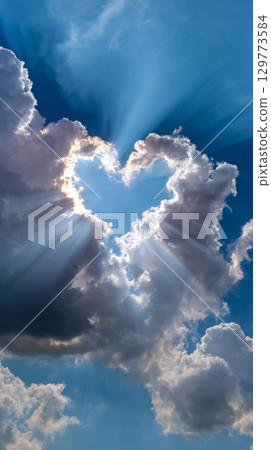 Heart-shaped cloud formation with sun rays on blue sky background. 129773584