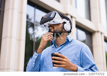 A man wearing a VR headset with coffee, looking at the building. Thinking about the future of technology and virtual reality. 129773722