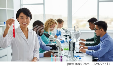 Diverse scientists working in a modern laboratory, with a smiling woman holding a test tube 129774517