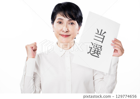 一位老婦人微笑著揮舞著拳頭慶祝，手裡拿著一張寫著她獲勝的紙 129774656