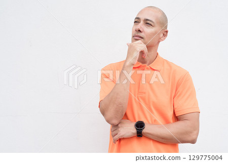 Bald Italian man in orange polo shirt thinking and looking up Bald Italian man in orange polo shirt thinking and looking up 129775004