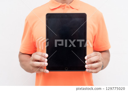Man in orange polo shirt showing digital tablet computer screen with copy space 129775020