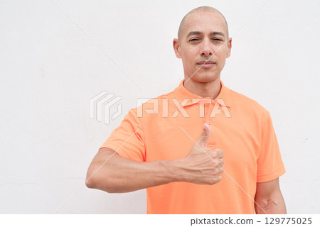 Bald Italian man in orange polo shirt giving thumb up gesture and looking at camera 129775025