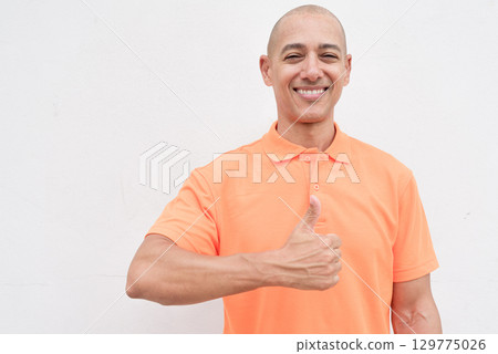 Happy bald Italian man in orange polo shirt giving thumb up gesture and looking at camera Happy bald Italian man in orange polo shirt giving thumb up gesture and looking at camera 129775026