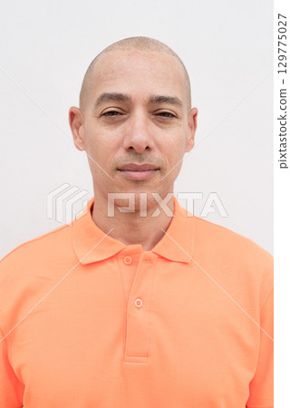 Bald Italian man face in orange polo shirt studio portrait against white wall looking at camera 129775027